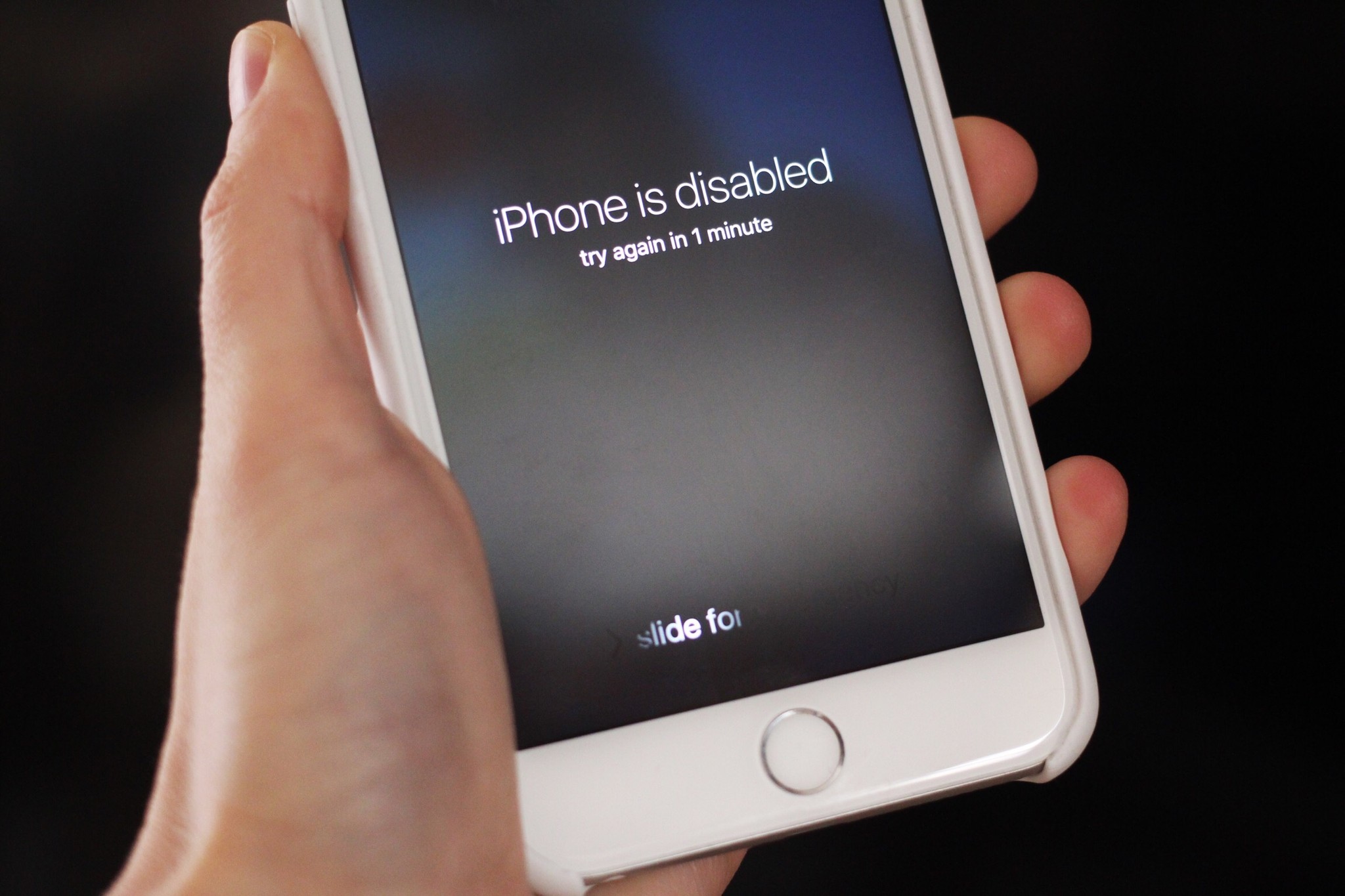  A person holding a phone that is locked and disabled with a message saying 'iPhone is disabled, try again in 1 minute'.