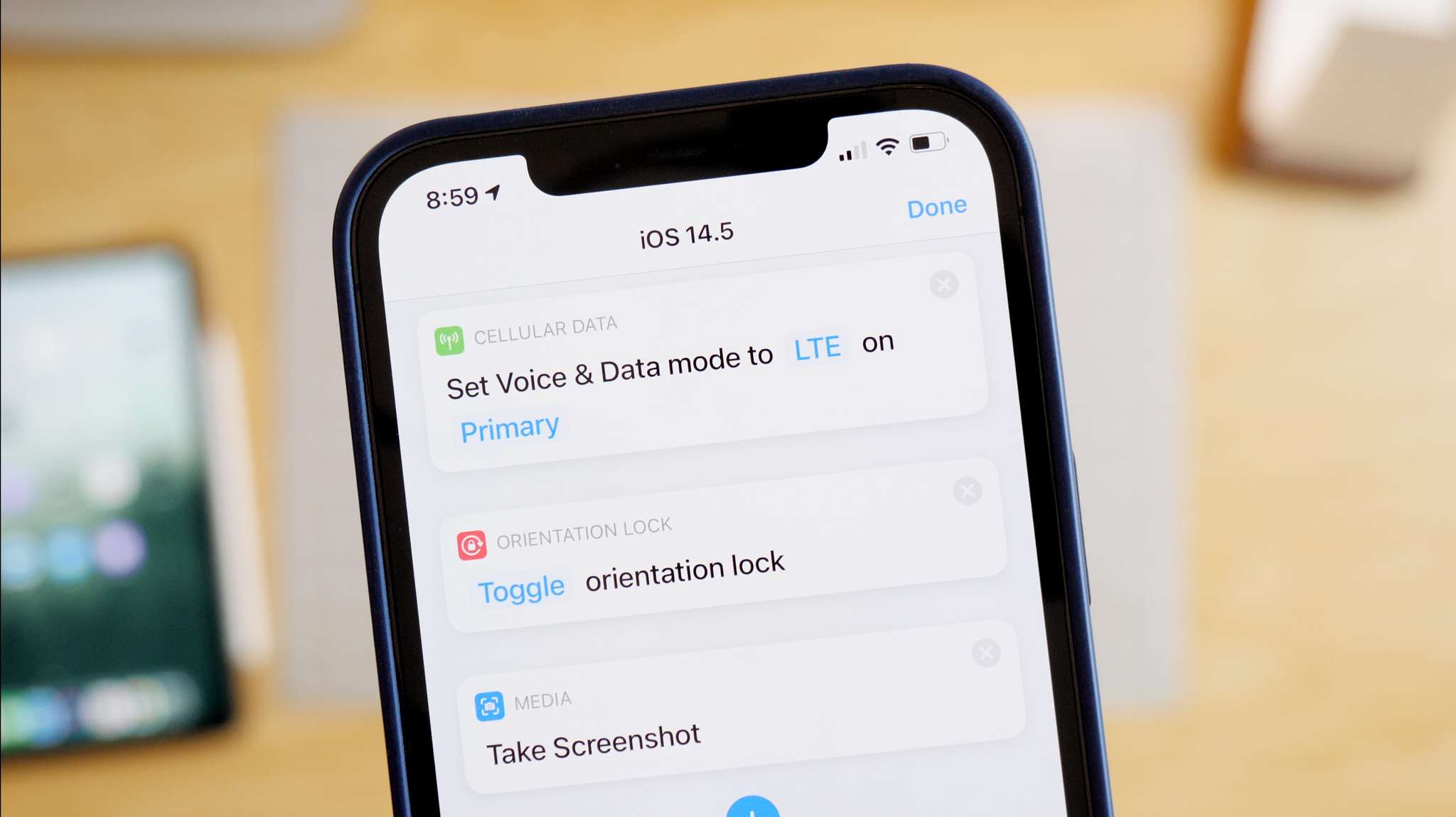 Hero photo of Shortcuts actions new in iOS 14.5 – Set Voice &amp; Data Mode, Set Orientation Lock, and Take Screenshot running on an iPhone above a desk with an iPad, Mac mini, and notecards on the surface