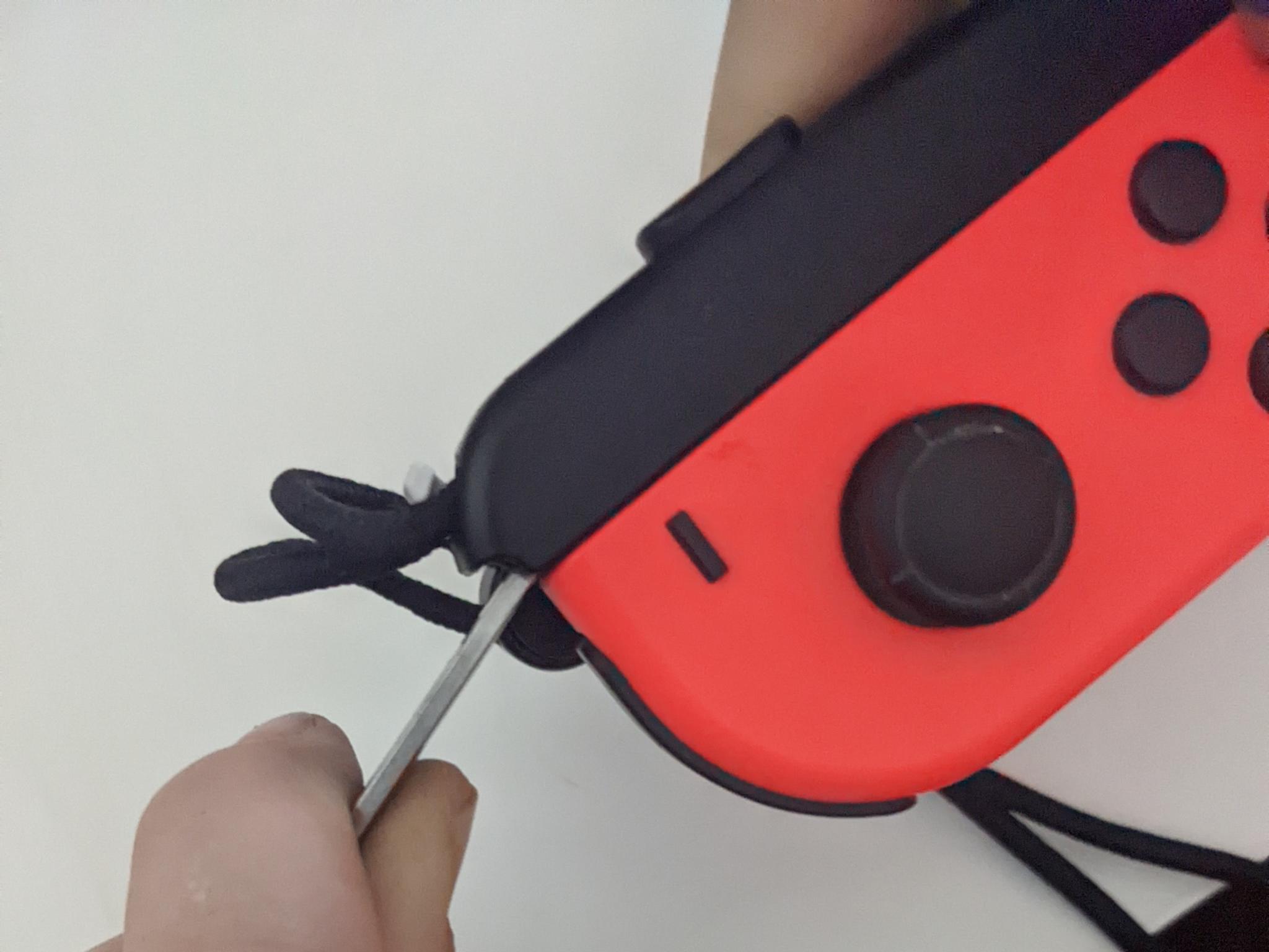 How to remove a stuck Joy-Con strap: push object toward prongs and away from the Joy-Con body with one hand