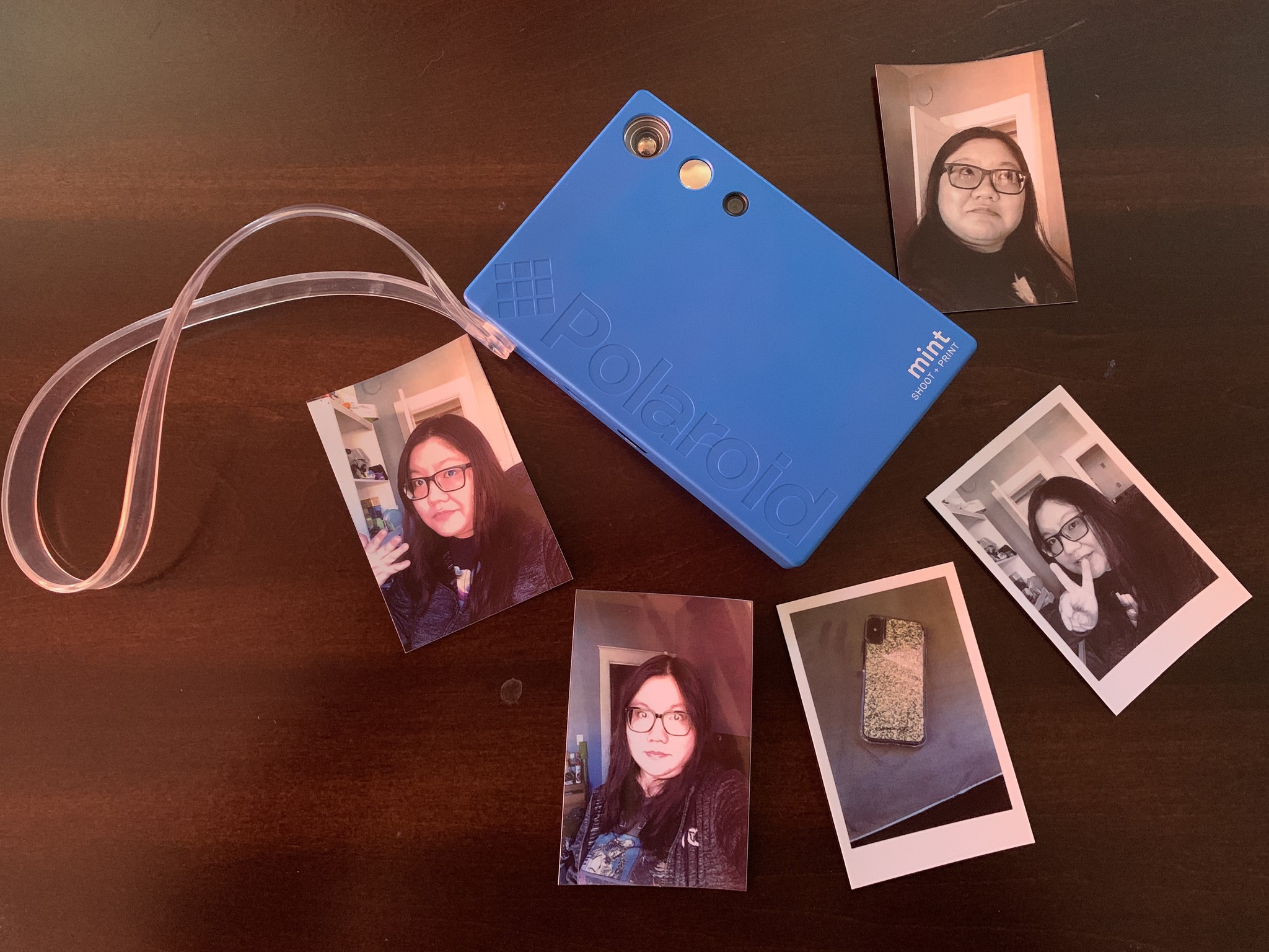 Blue Polaroid Mint Camera Printer on wooden table surrounded by printed photos of Christine Chan