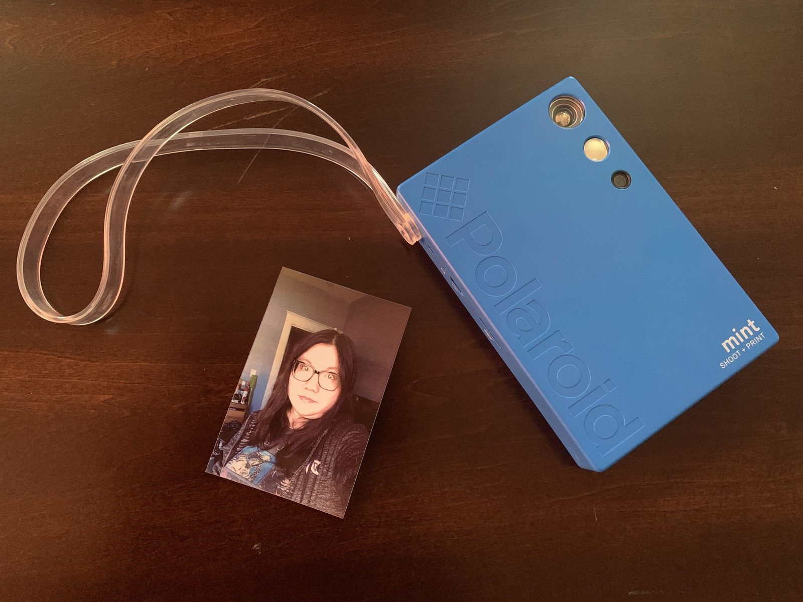 Blue Polaroid Mint Camera & Printer on wooden table with a printed selfie of Christine Chan