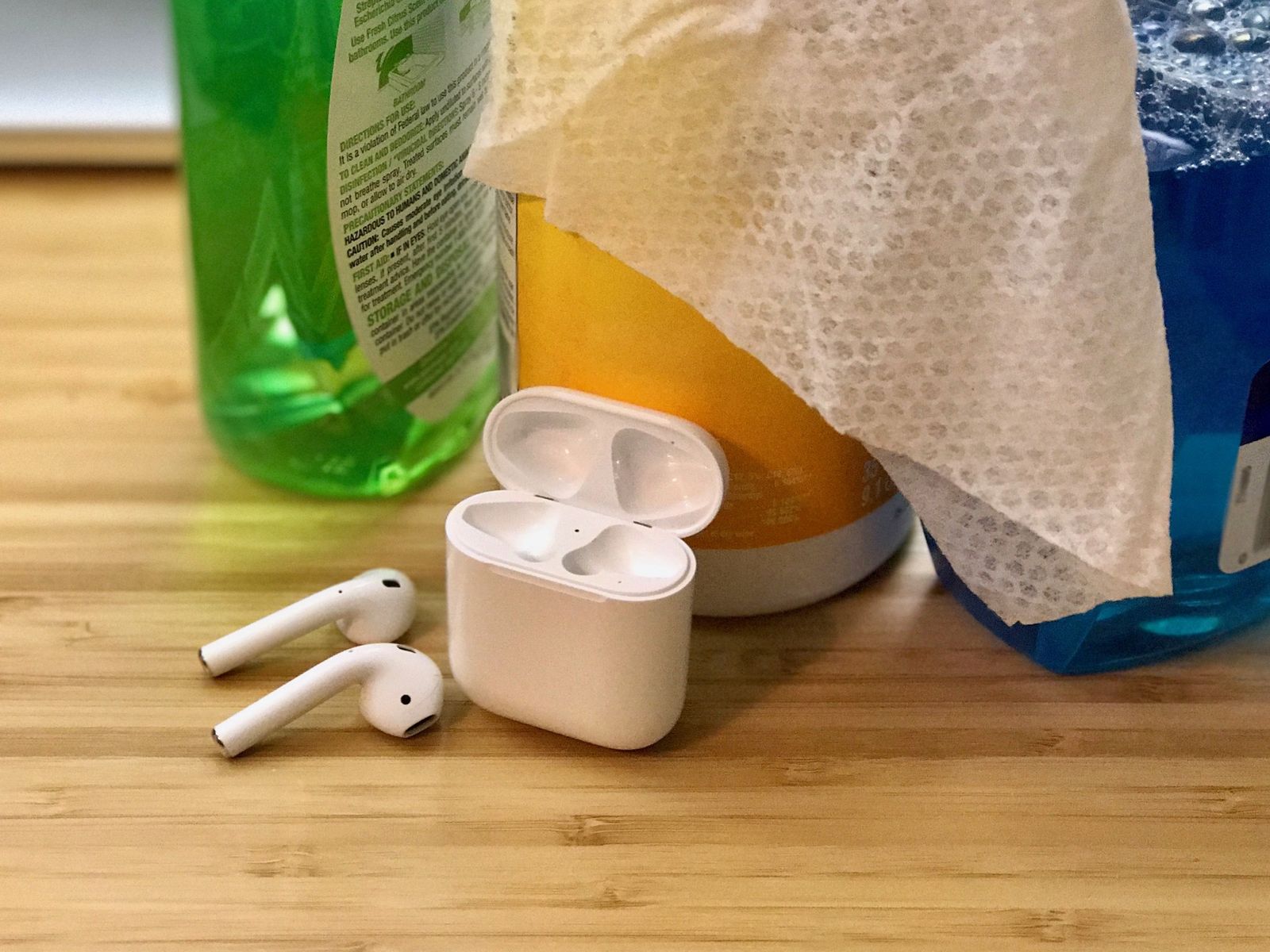 AirPods rest in front of various cleaning products.