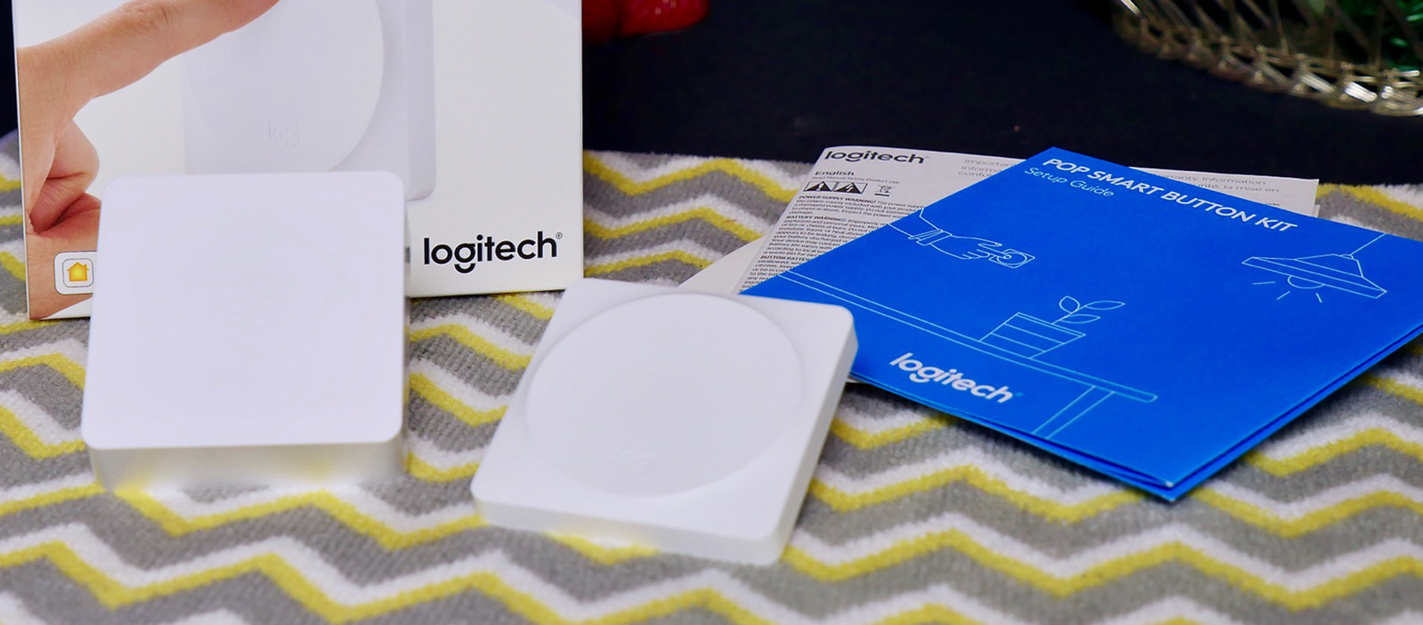 The Logitech POP Smart Button sits beside the HomeKit-enabled POP bridge, a startup guide, and the box in which everything came.