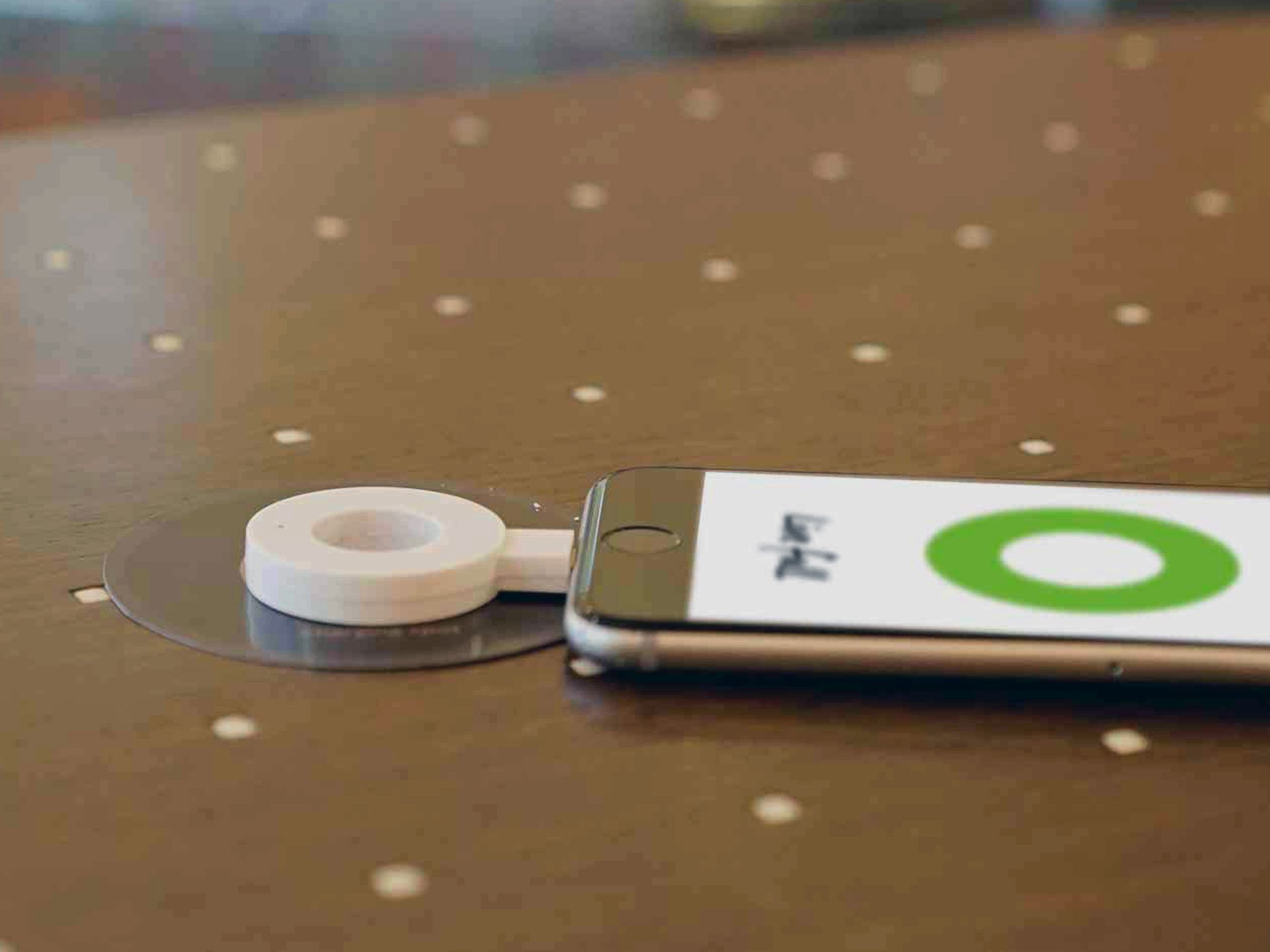 A Powermat charging ring is shown plugged into an iPhone. It&#39;s centered atop a Powermat charging pad thereby charging the phone.
