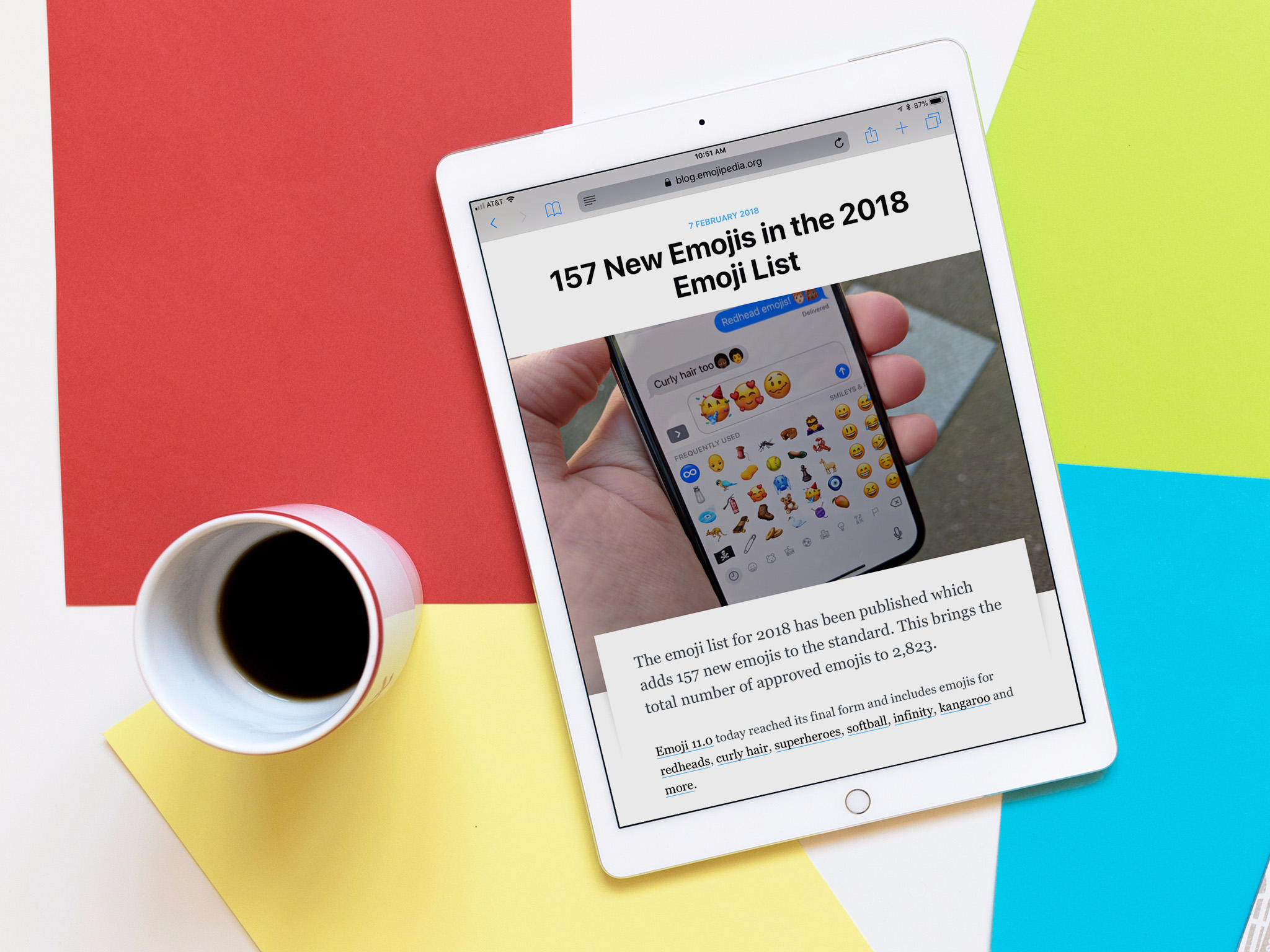 The emojipedia website is shown on an iPad Pro which rests next to a cup of coffee