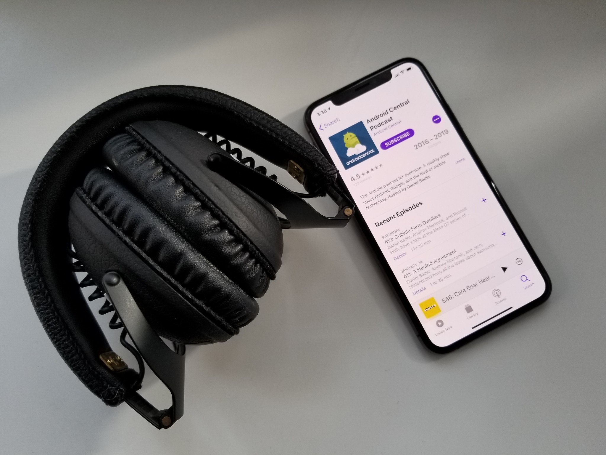 iPhone XS with Apple Podcasts showing Android Central podcast page on a white table next to black headphones